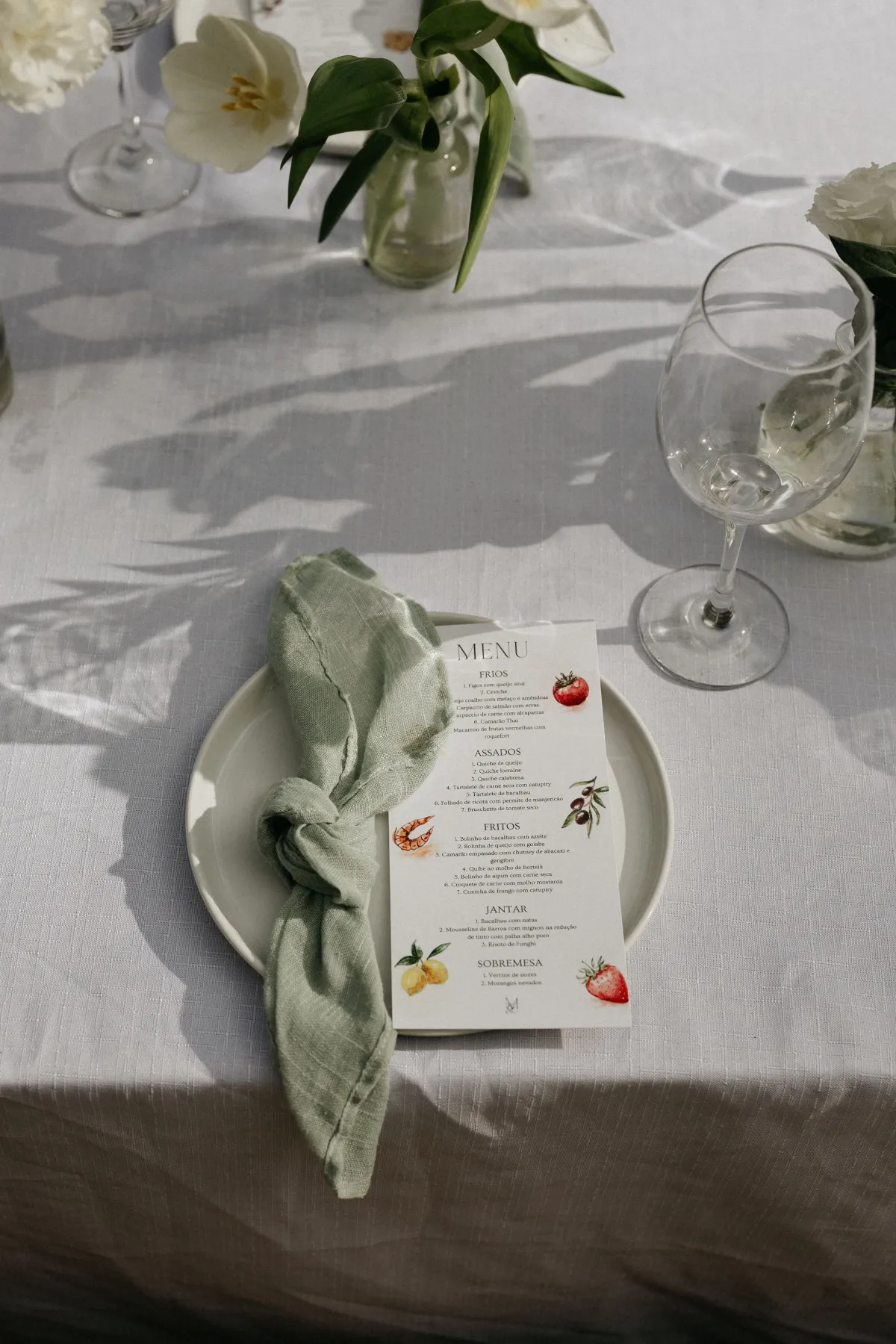 Menu de casamento ilustrado num prato, com guardanapo de linho e tulipas brancas