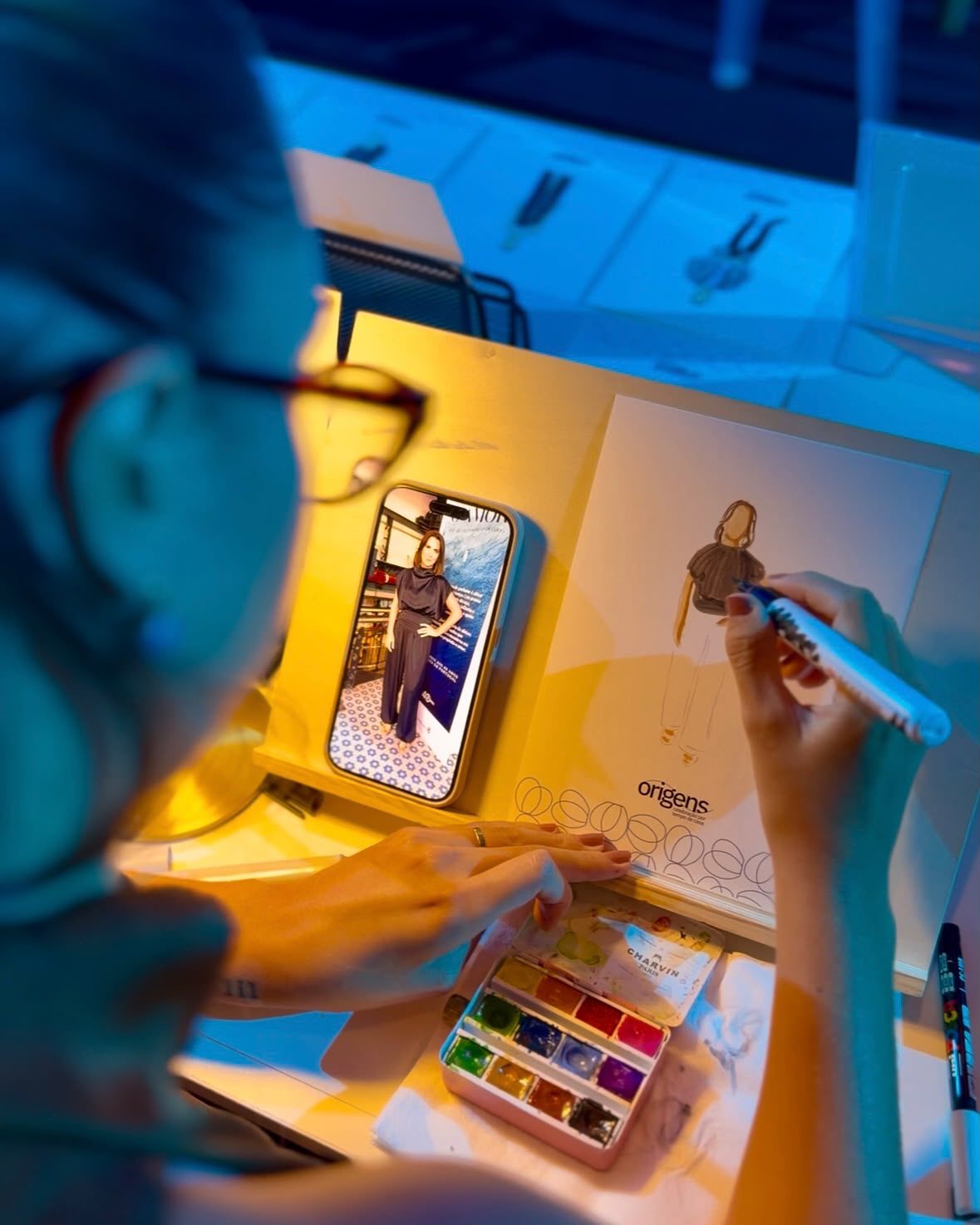 Luíza pinta um retrato a partir de uma foto no telemóvel, com a paleta de aquarela na mesa · Souluarte