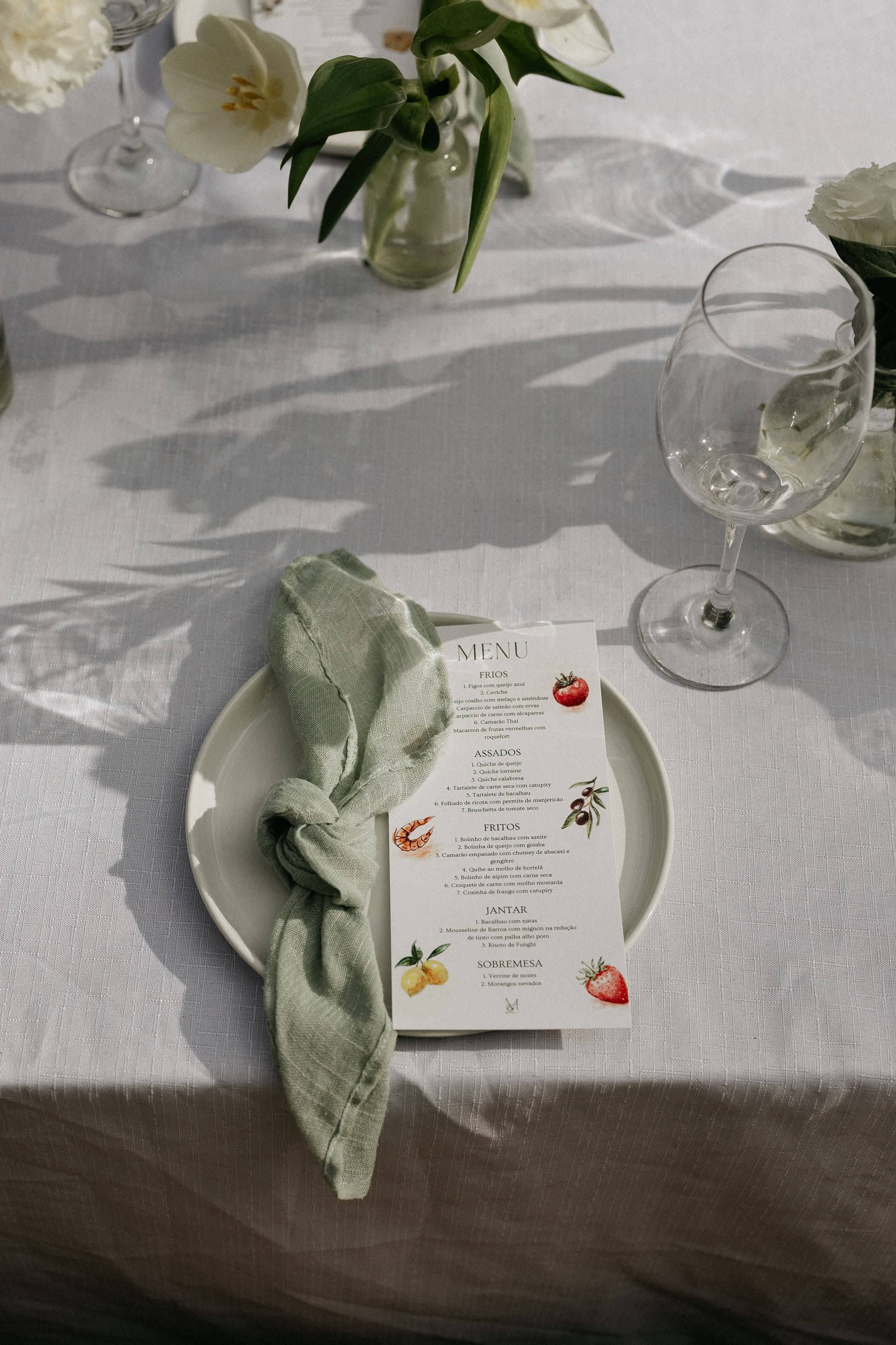 Menu de casamento ilustrado num prato, com guardanapo de linho e tulipas brancas