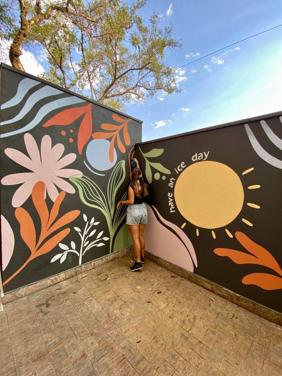 Outdoor courtyard mural with bold flowers and a sun, “have an ice day” · Souluarte