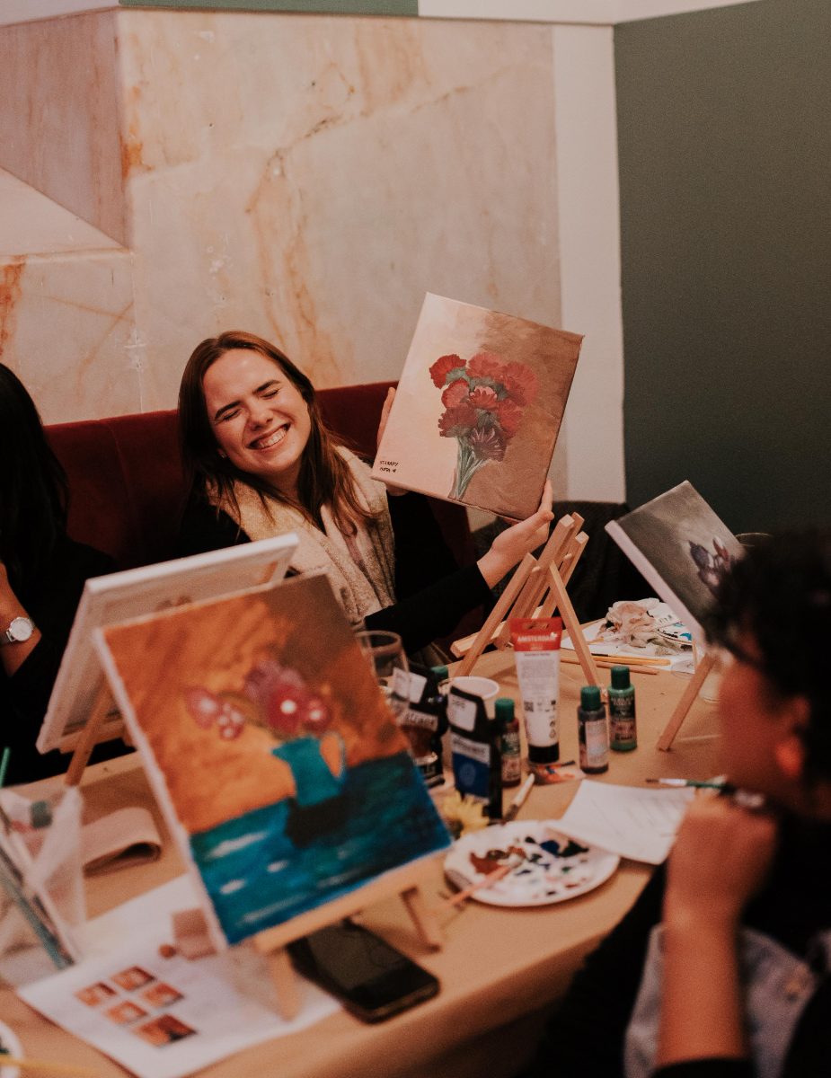 Participant laughing as she holds up her finished carnation painting · Souluarte